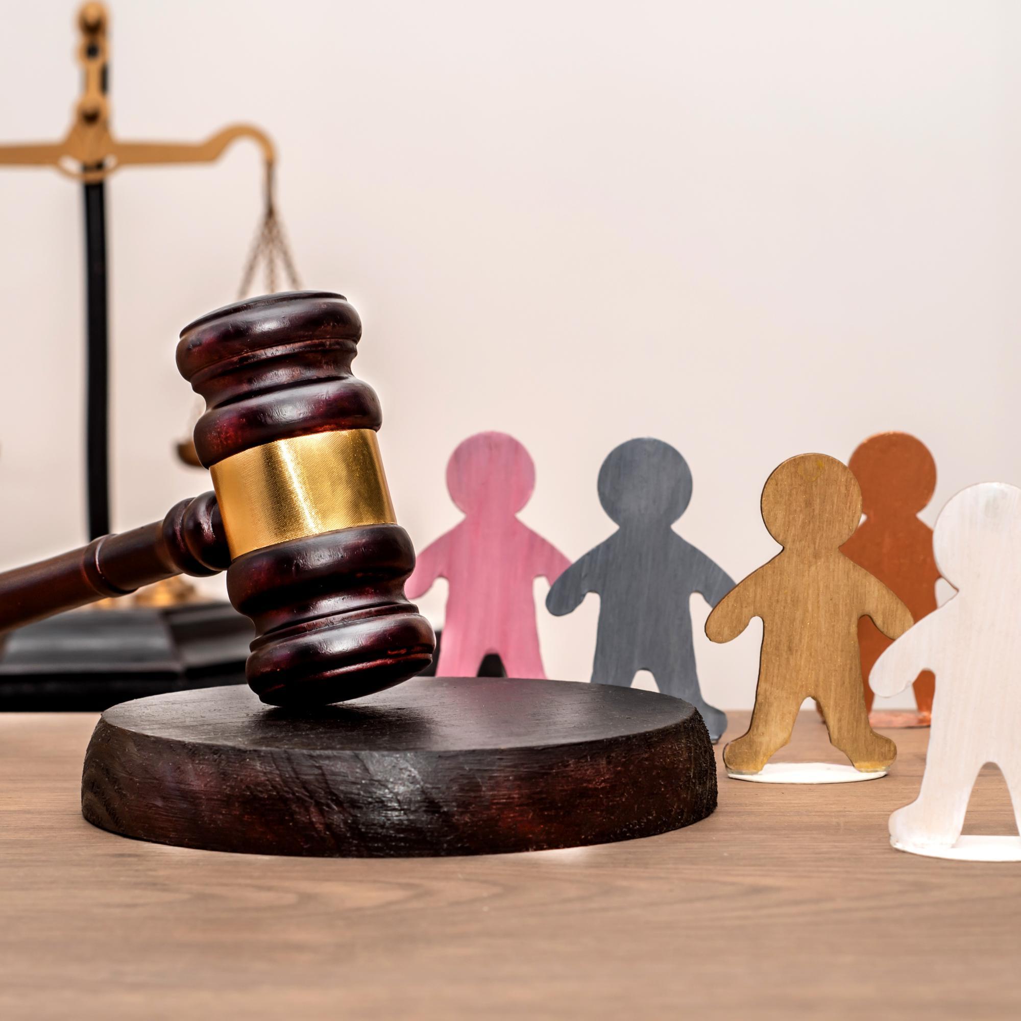 Judge's gavel next to human figures and scales of justice in the background