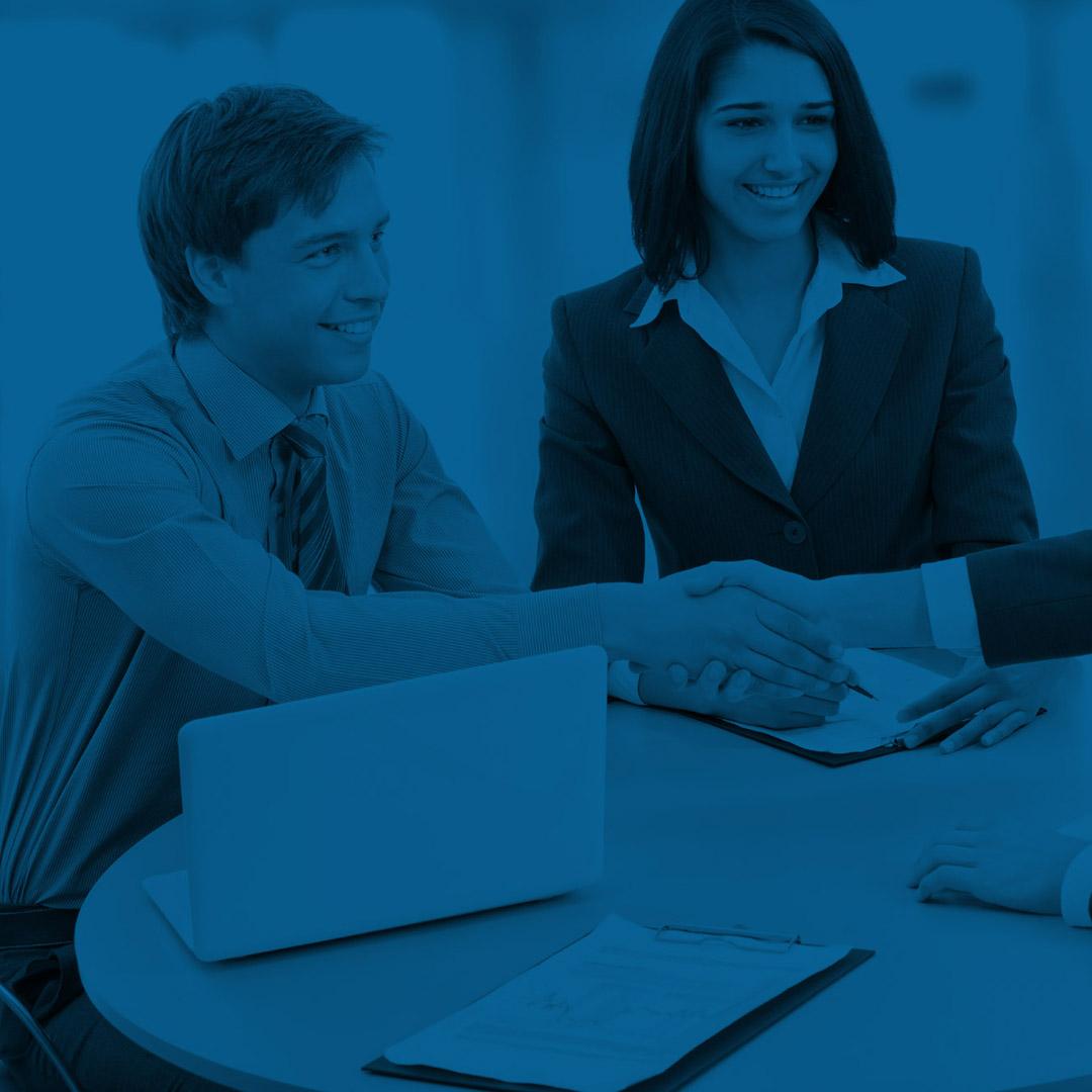 Young professional man and woman sitting at a table shaking customer's hand