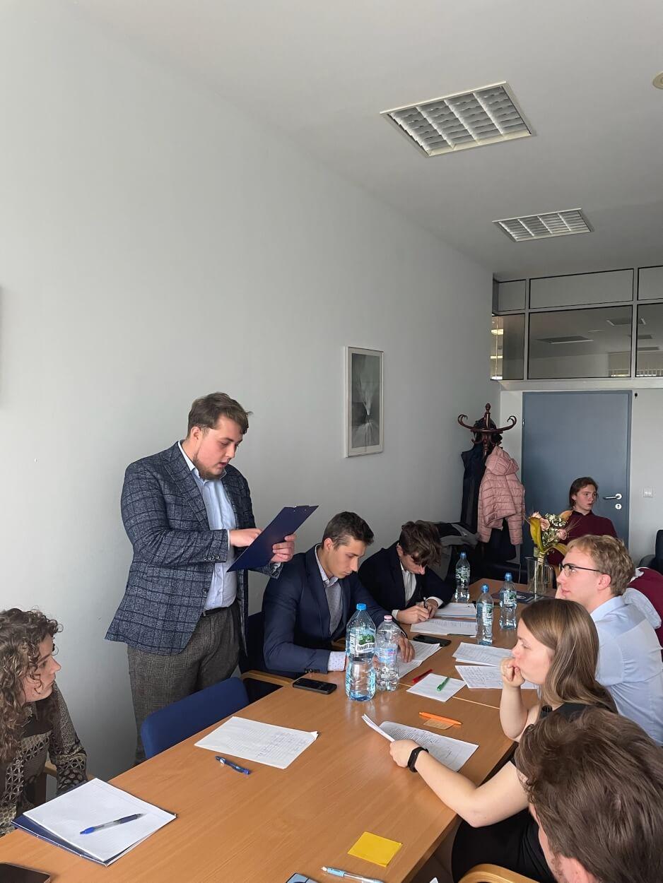 Group of students during a debate sitting by a table and taking notes while Przemysław Majewski is speaking.