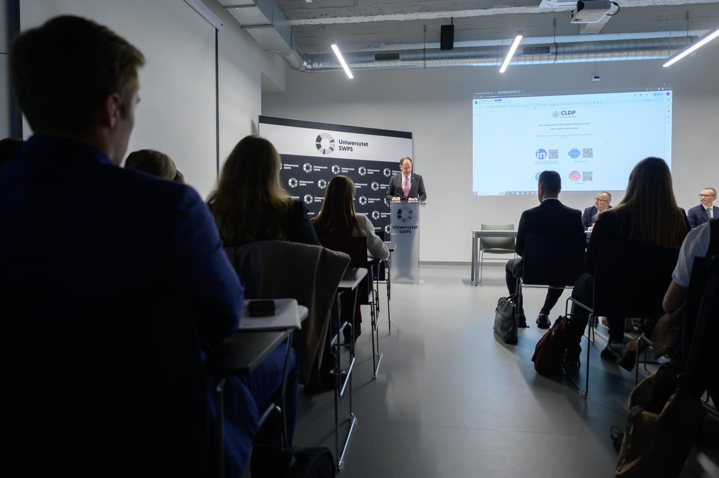 Rear view of the audience at the opening of the Vis Moot Bootcamp at SWPS University in Warsaw, Poland, with U.S. Ambassador Mark Brzezinski speaking in the background.