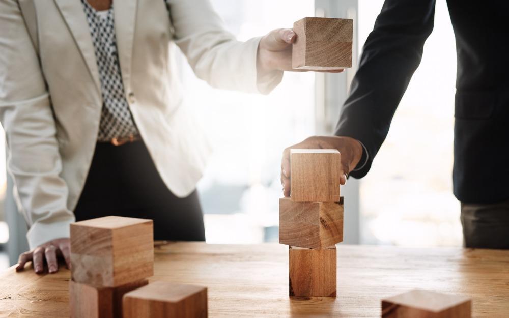 man and woman building tower of square wooden blocks
