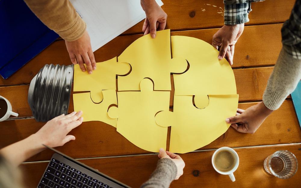 multiple hands putting together large lightbulb puzzle